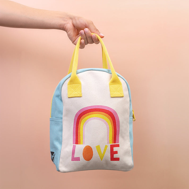 Small backpack with a rainbow and 'LOVE' text held by a hand against a peach background