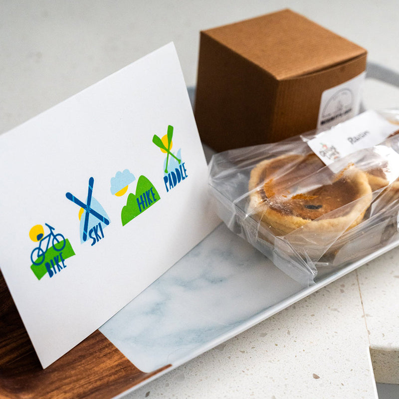 Packaged pastries with a card featuring outdoor activity symbols on a wooden surface.