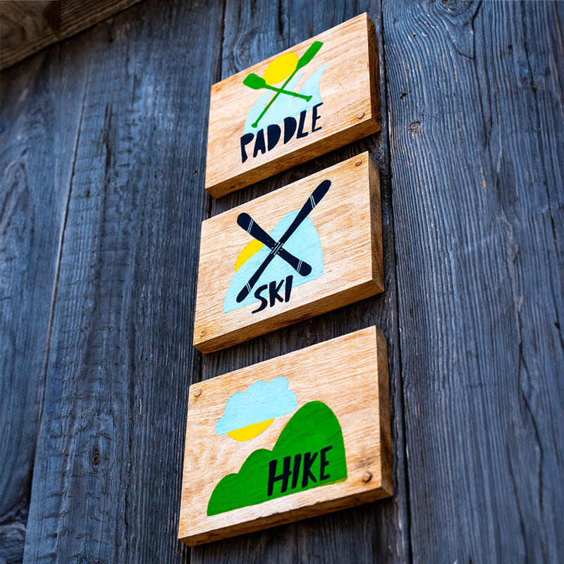 Three wooden blocks with paddle, ski, and hike illustrations on a wooden background