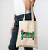 Person holding a tote bag with a cartoon design of animals on a bench.