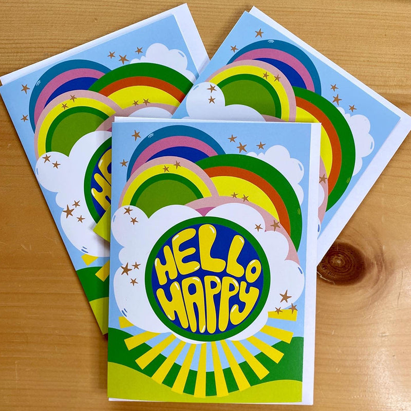 Three colorful greeting cards with rainbow designs and 'HELLO HAPPY' text on a wooden surface.