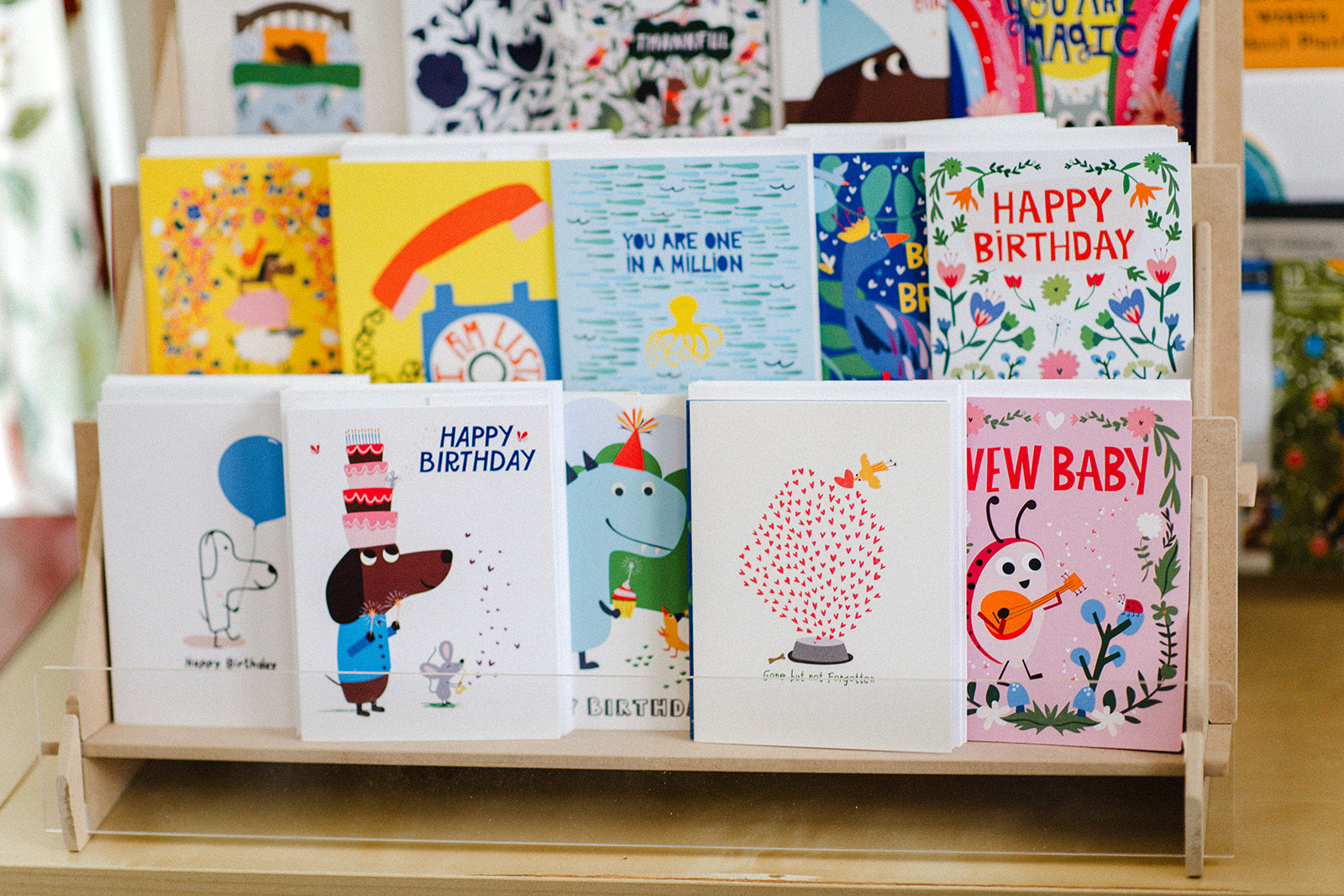 Assorted illustrated greeting cards on a wooden display stand.