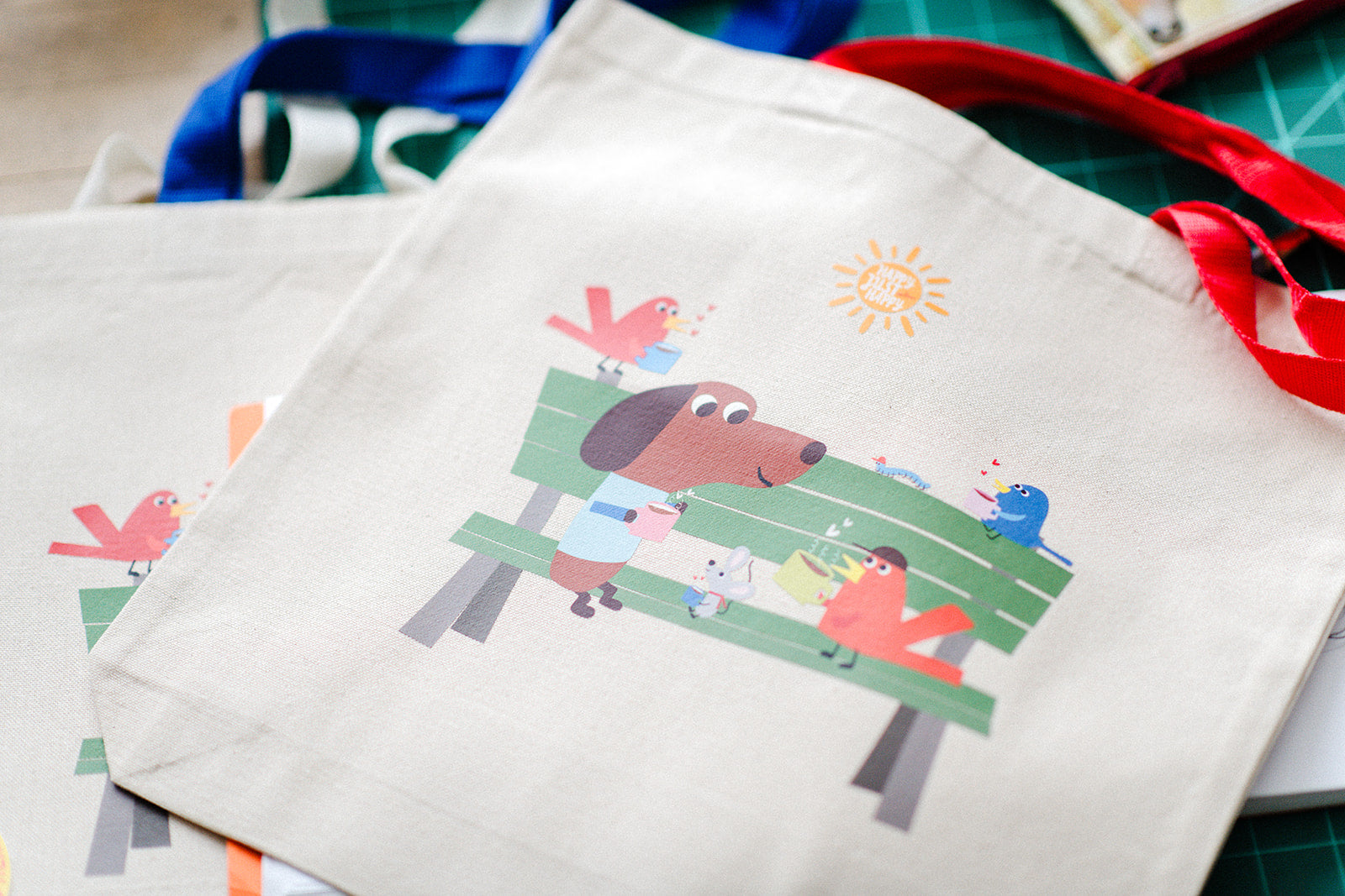 Canvas tote bag with cartoon design of a dog on a bench, birds, and a sun.